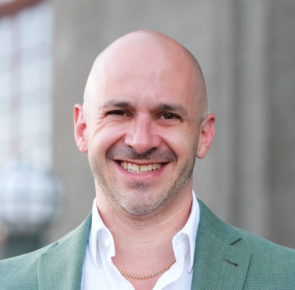 Ed Essey smiling, bald man in a green suit and white shirt